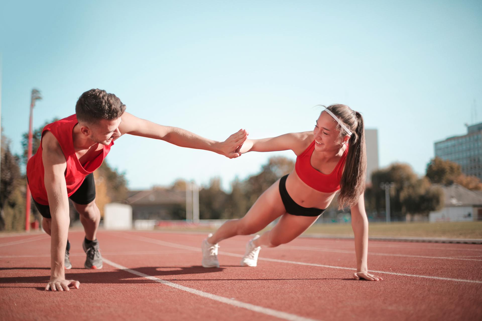 Man and woman in red and black running outfits high-five while holding a plank pose.