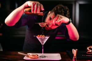 Professional bartender preparing martini with olives at bar counter. Dry vodka martini, cocktail served in restaurant, pub and bar. Long drink cocktail concept
