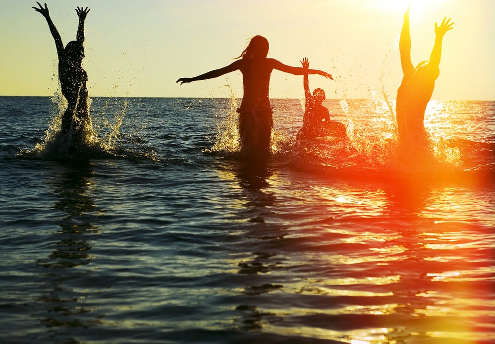 Silhouettes of young group of people jumping in ocean at sunset