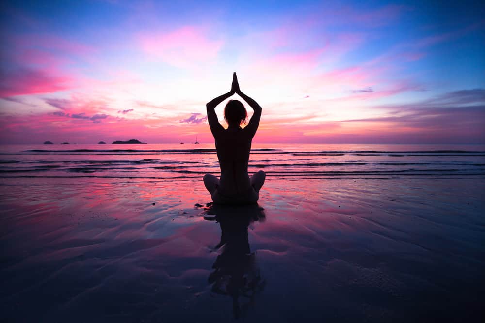 Sunset yoga woman on sea coast.