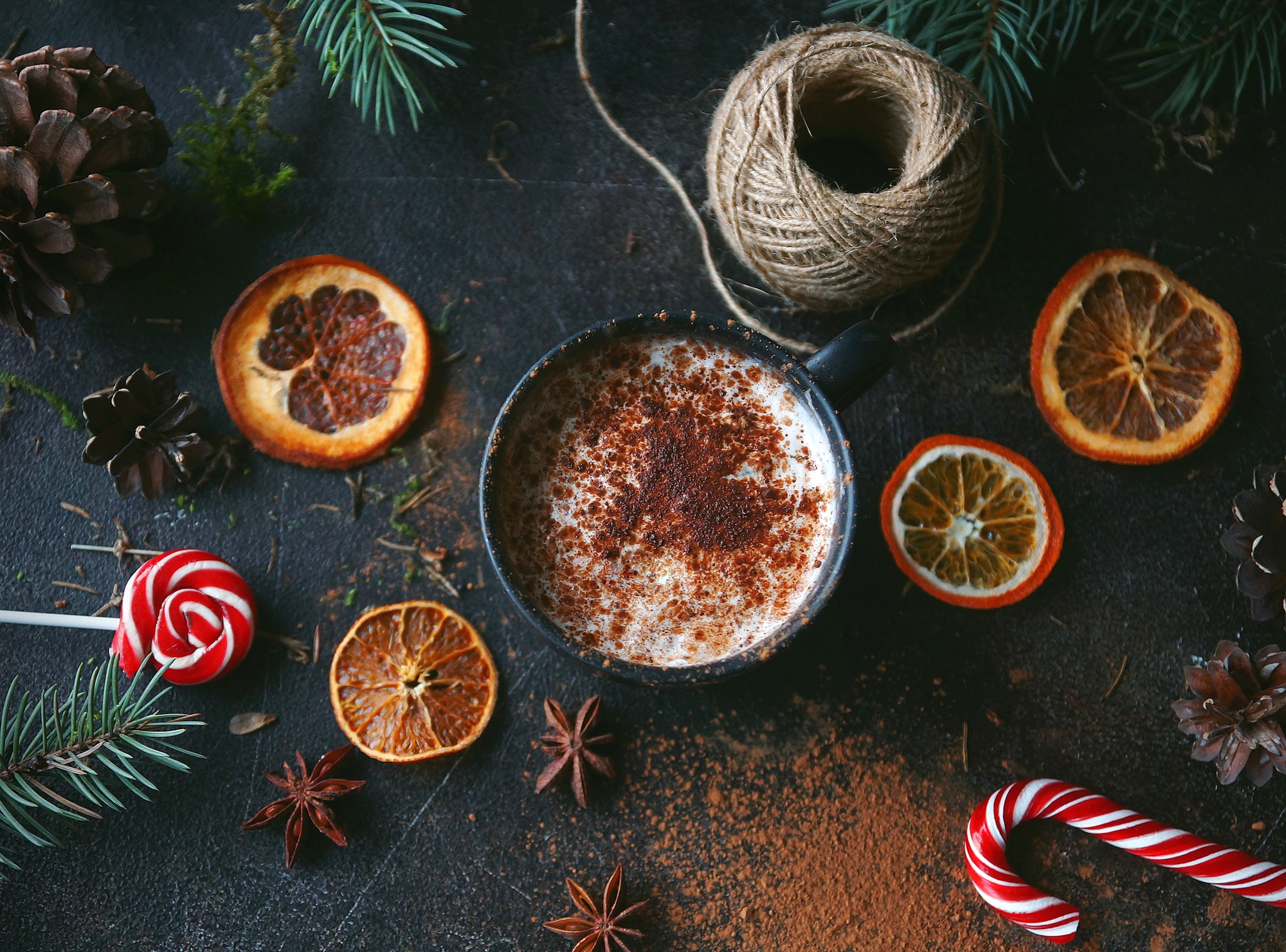 Christmas hot chocolate in a black cup with caramelized oranges, fir branches and candy cane on dark background, Selective focus