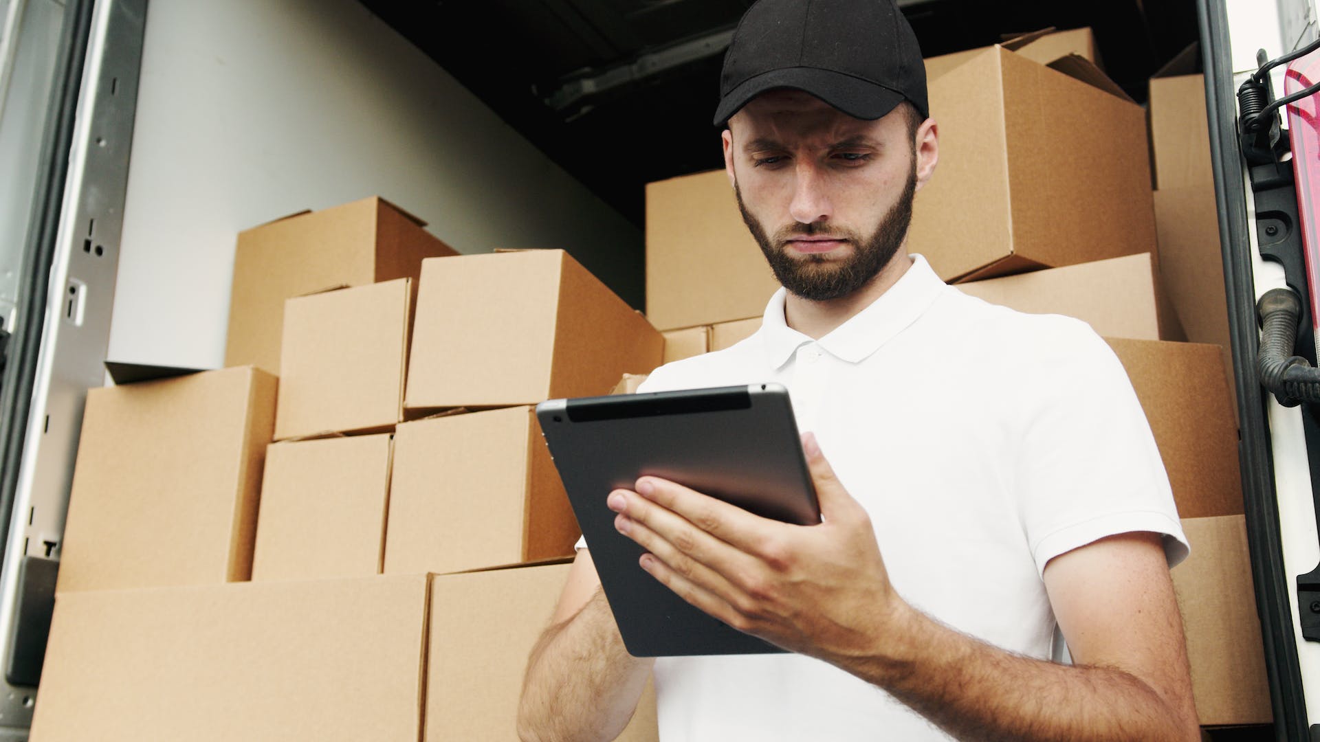 Man looking over checklist while frowning with multiple stacks of cardboard boxes packed into a moving van in the background