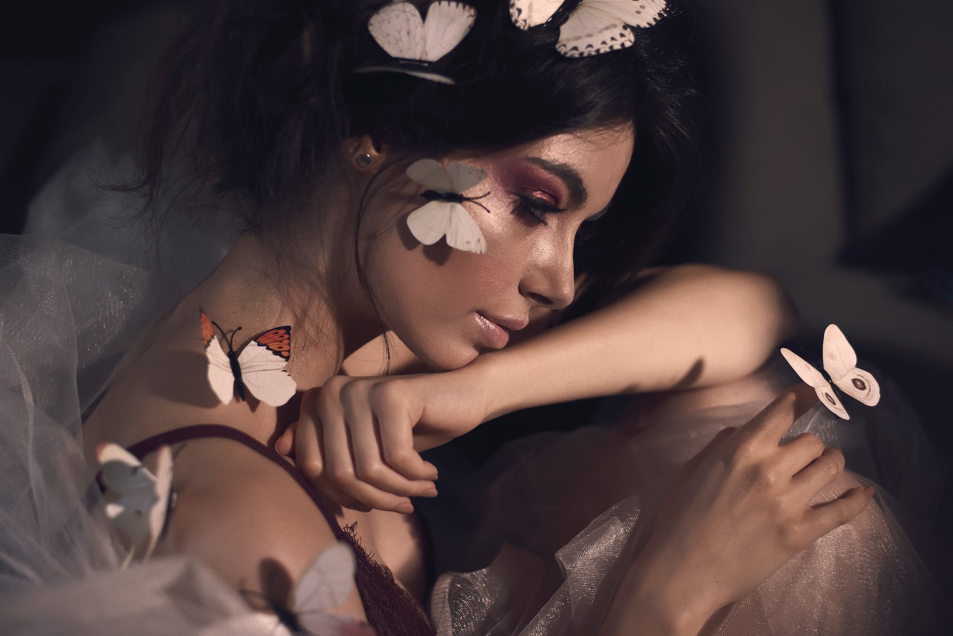 Ethereal woman covered in butterflies sits contemplating a butterfly on her finger