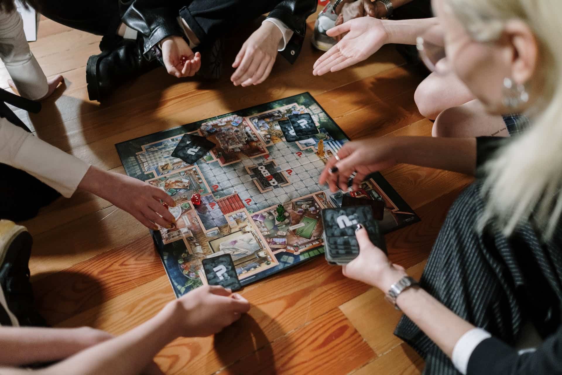 Cluedo game sits in the center with hands reaching out for the pieces.