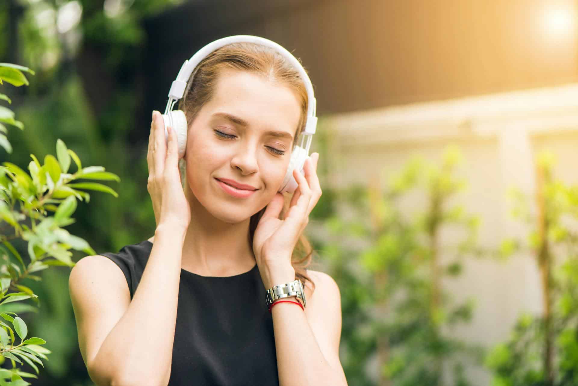 Woman listening to music with a blissful expression surrounded by greenery