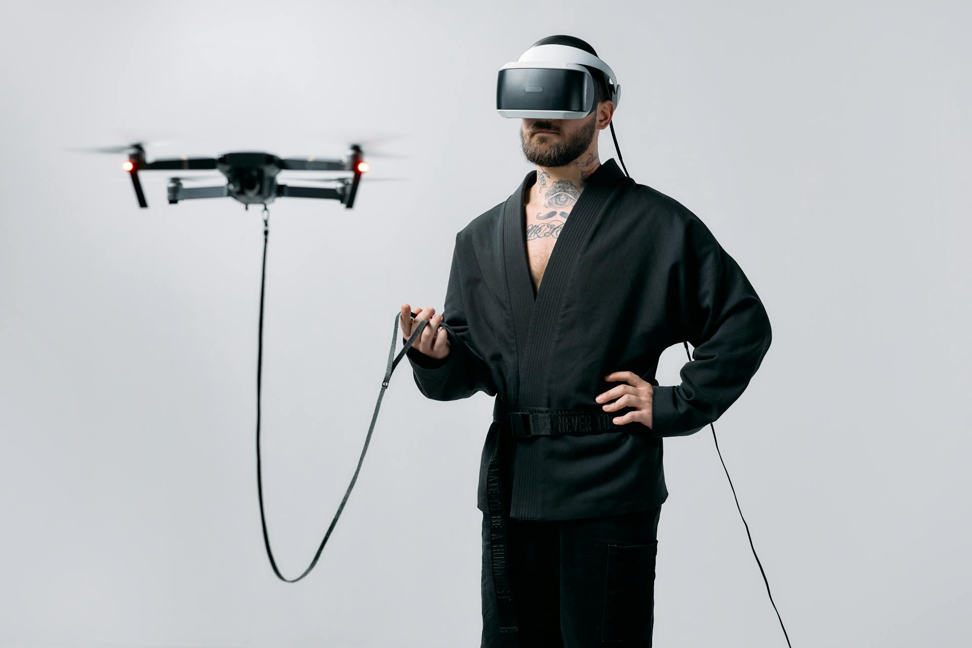 Man in black bath robe wearing VR goggles while walking a flying drone on a leash