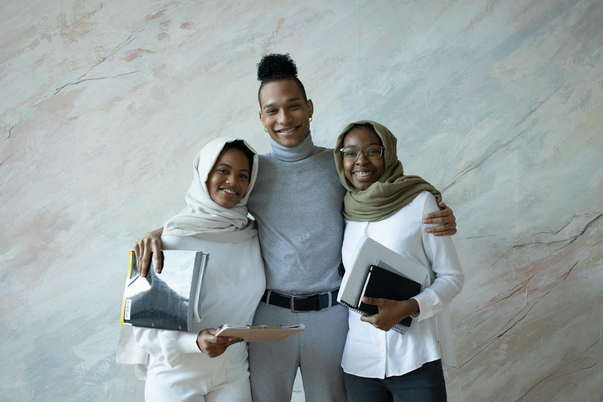 Two women and a man all in semi-professional attire smile for the camera in a relaxed group half-hug while holding business documents.