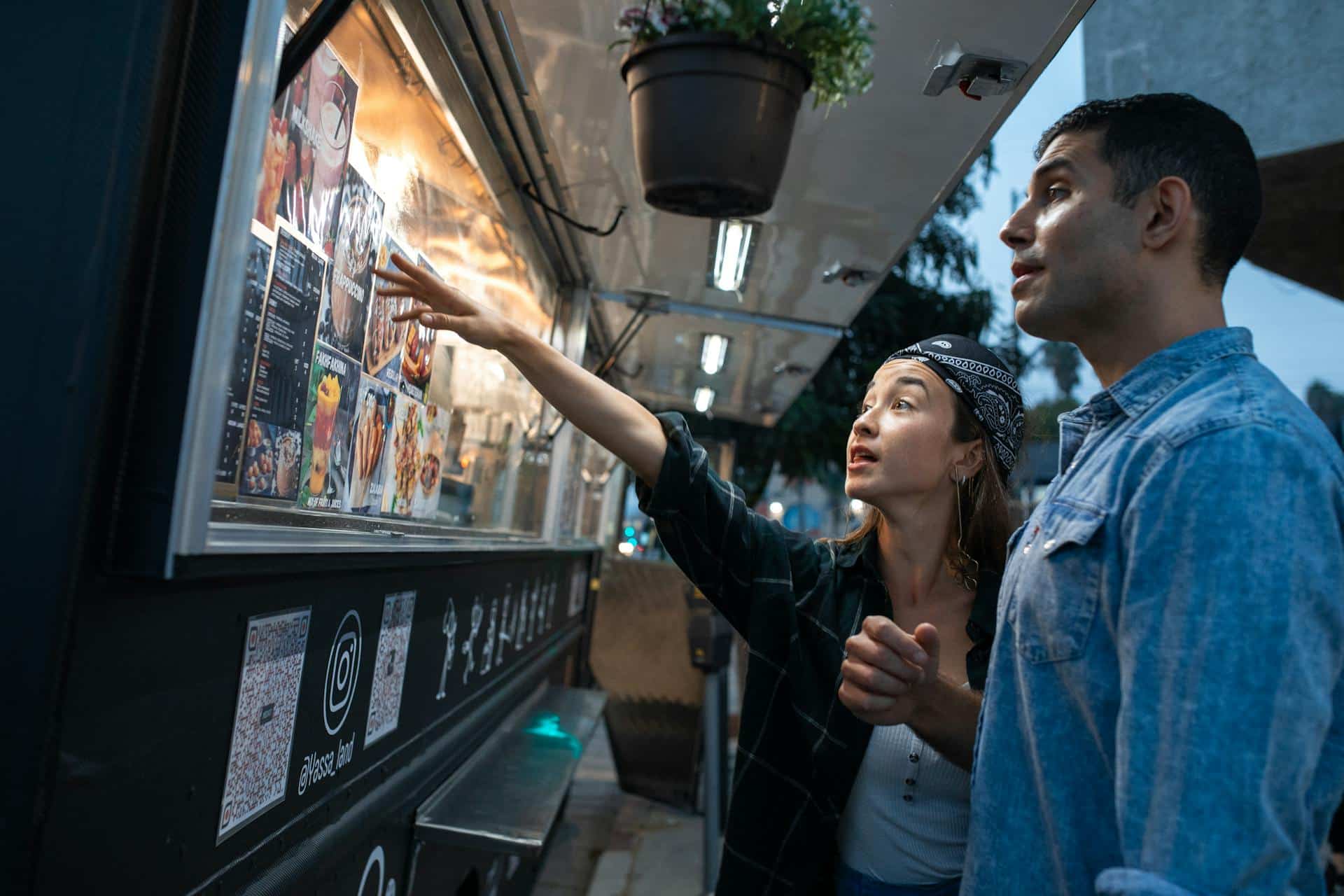 Man and woman discuss food truck's menu in the twilight.