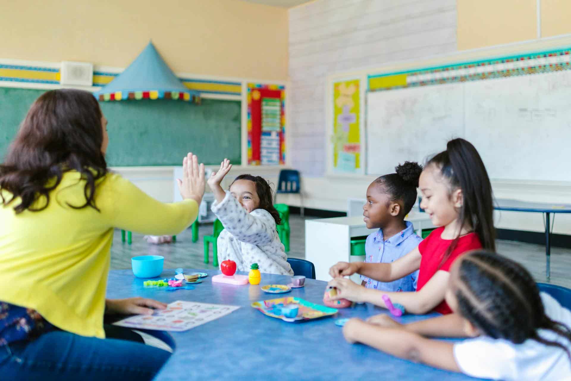 Little girl in a group if children high fives teacher.