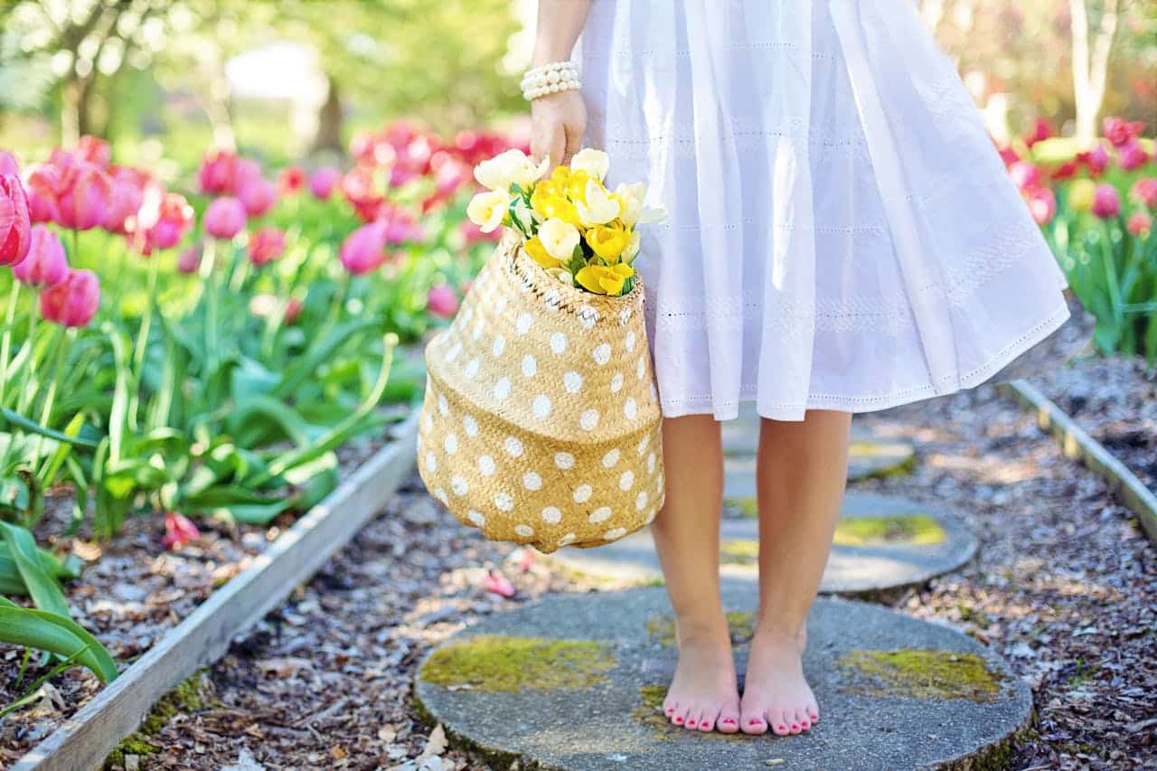Low to the group shot of a person in a skirt holding a basket of flowers with a garden in the background