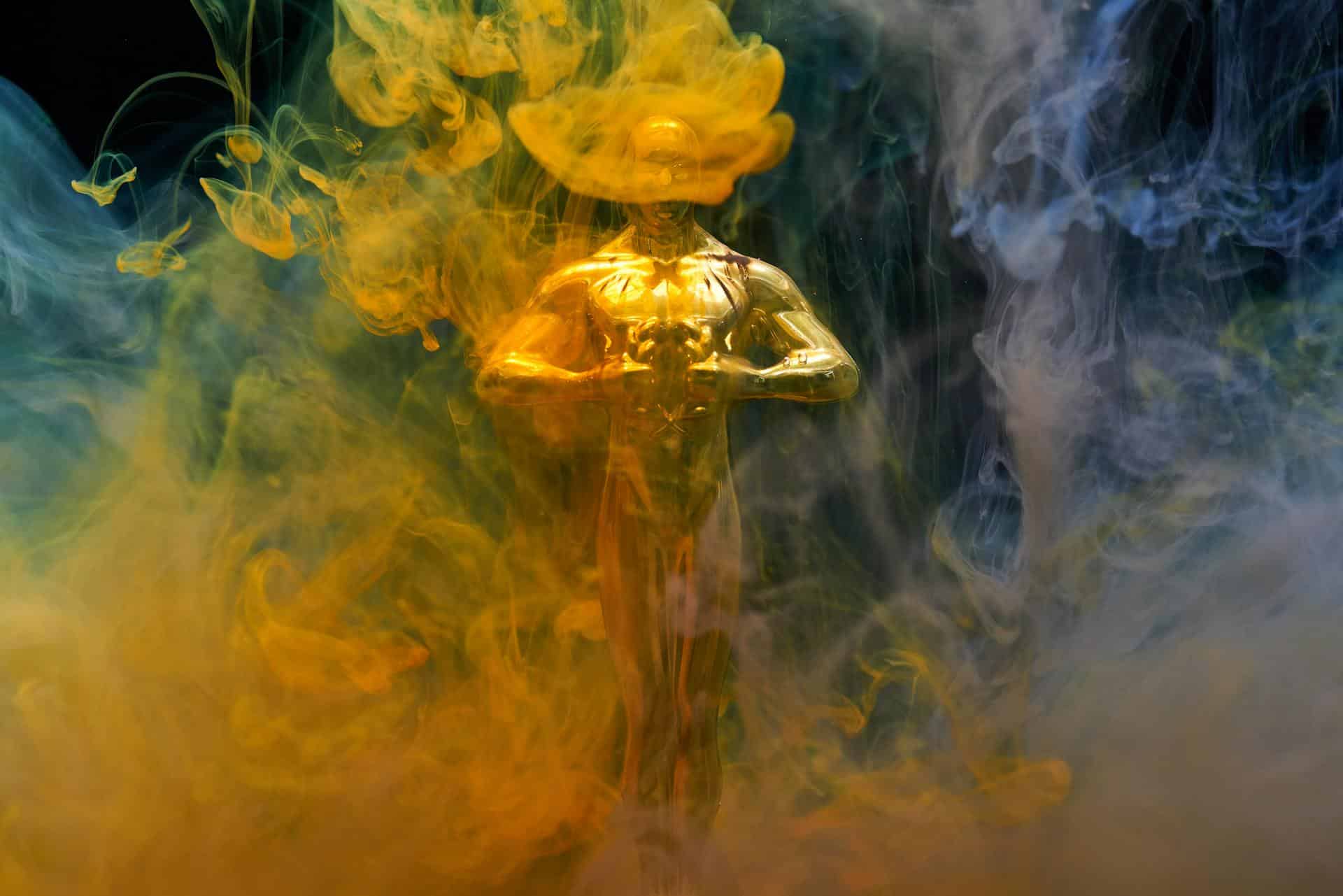 A golden Oscar award partially obscured by colored smoke.