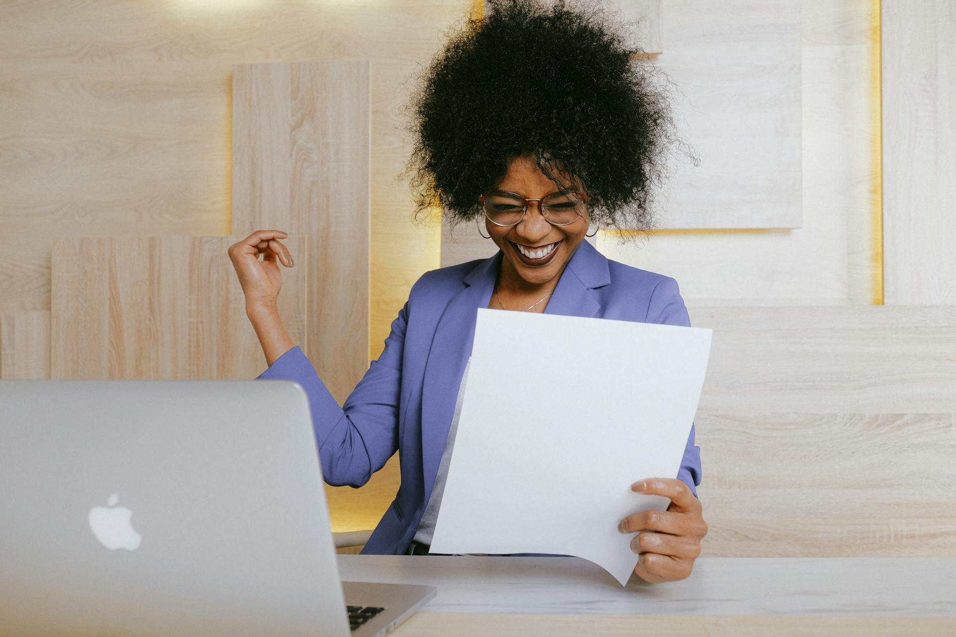 Woman in a suit smiles with joy and pride while reading a document.