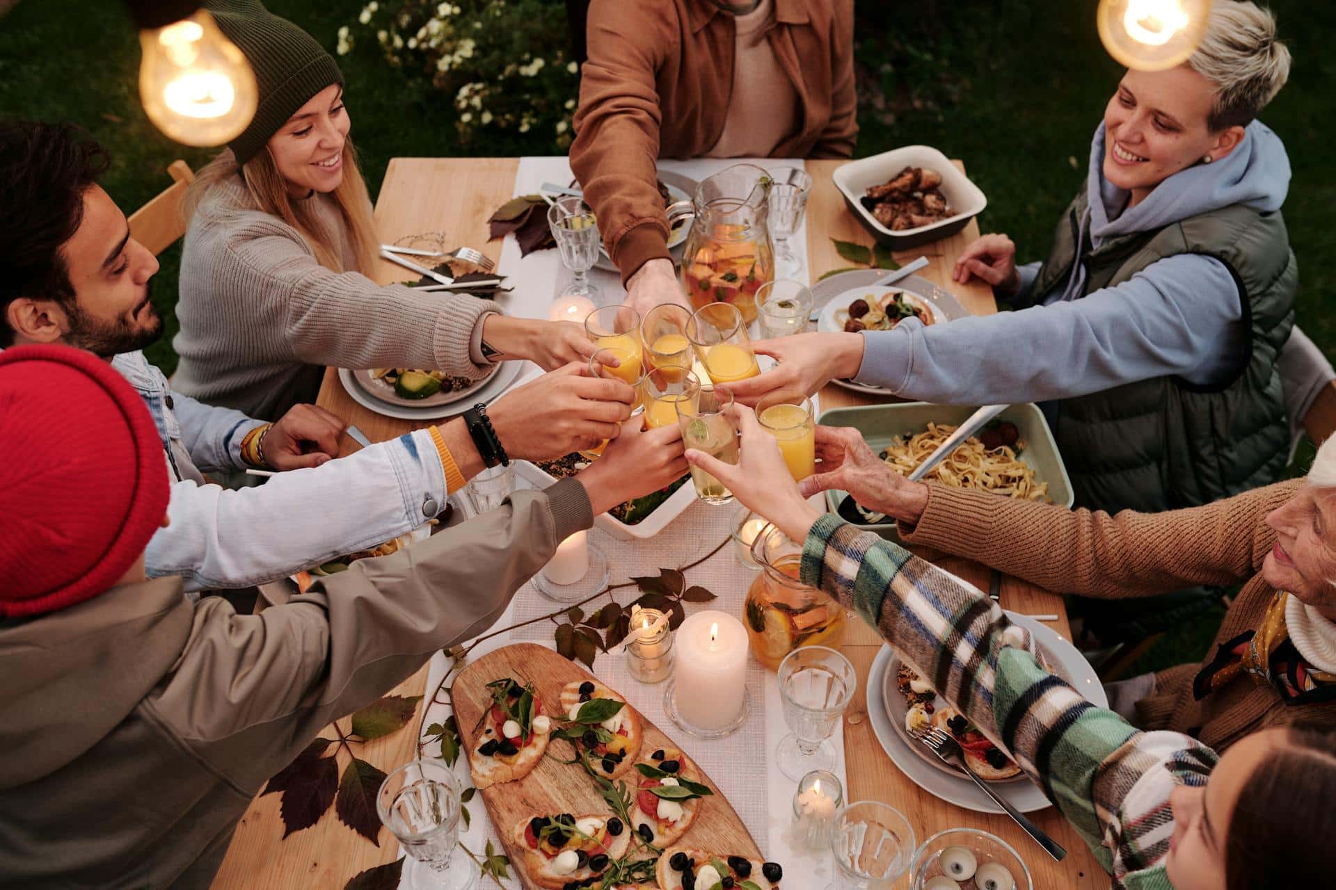 A group of people cheers over a Thanksgiving dinner outdoors.
