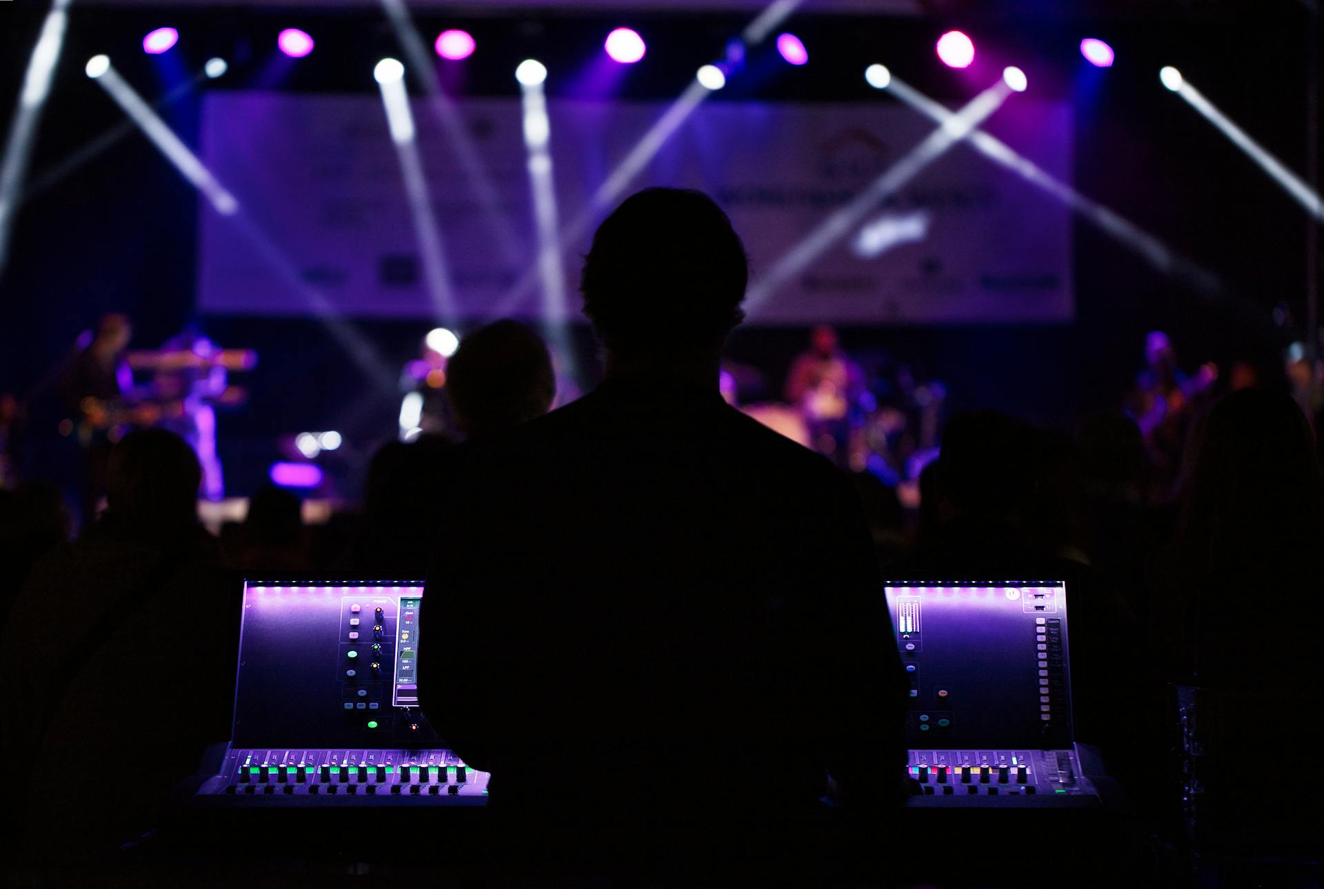 Silhouette of a man playing electronic music with a purple backdrop of club lights.