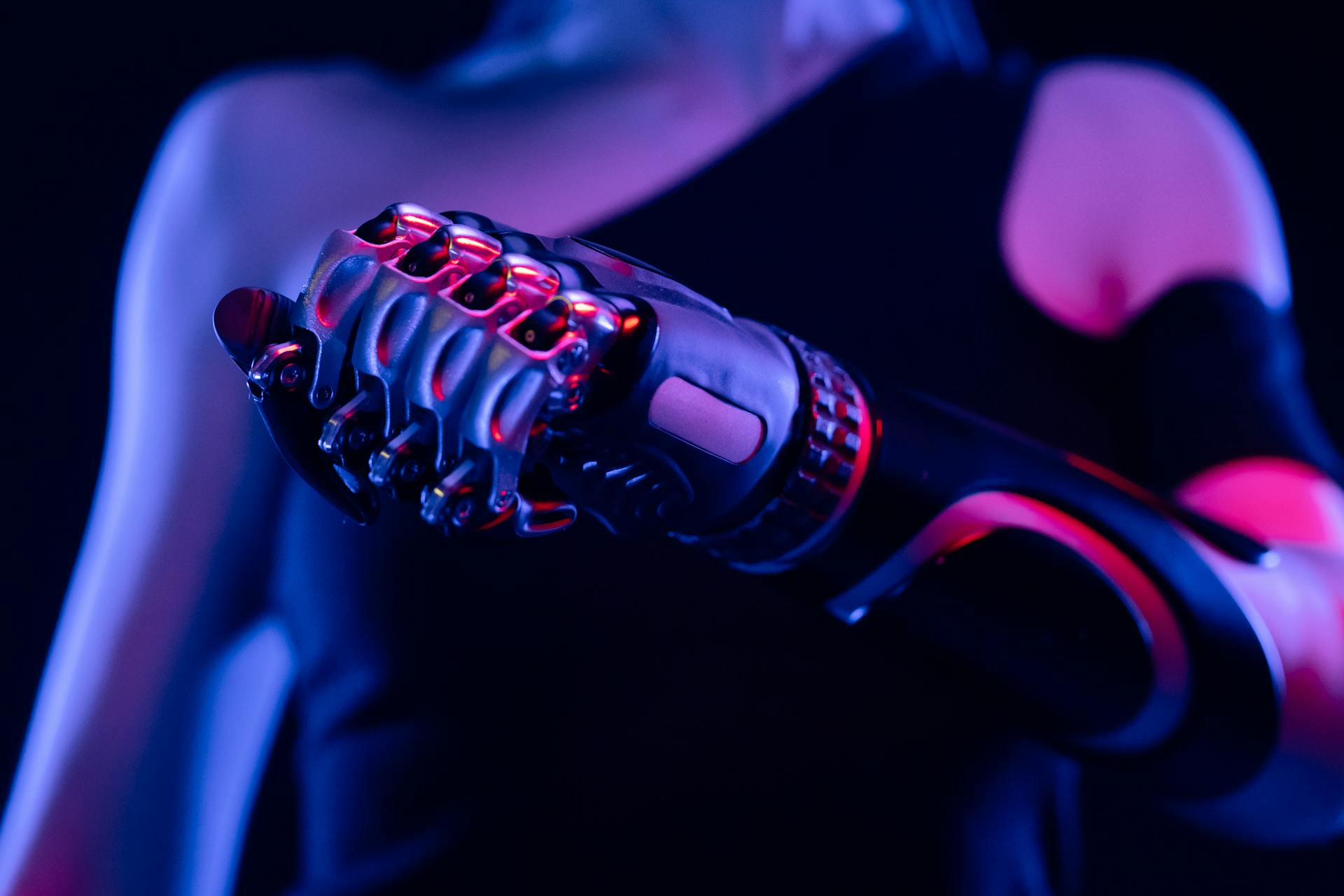 Closeup of a bionic hand outlined in neon pink and blue light.