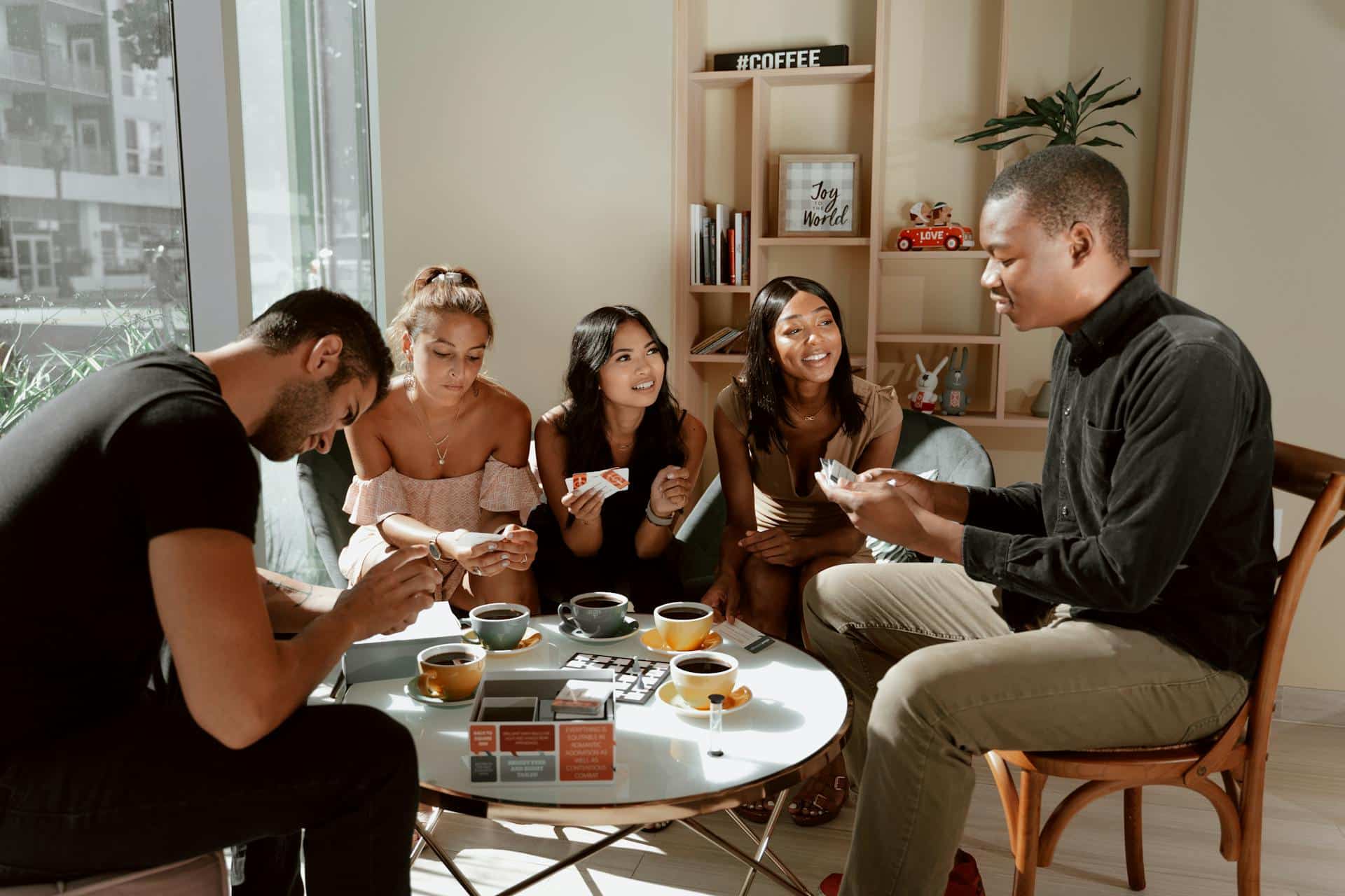 A group of people sit around a cafe table while drinking coffee and playing a game