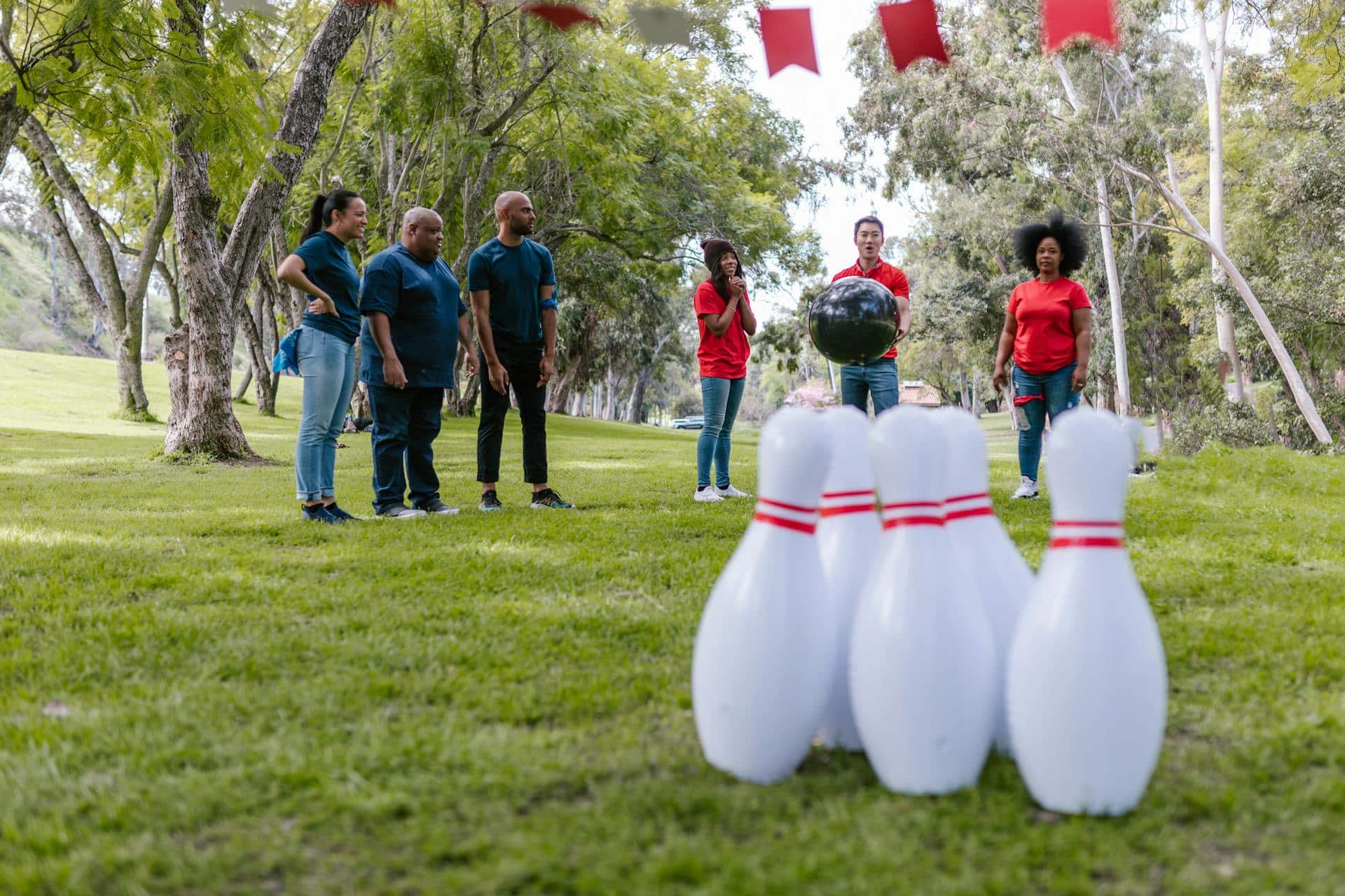 A team of people in a park play a game of bowling using oversized blow-up game set.