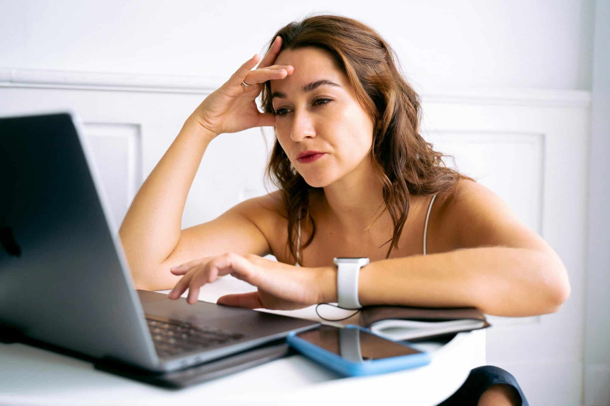 Woman working on laptop with hand on forehead looking frustrated