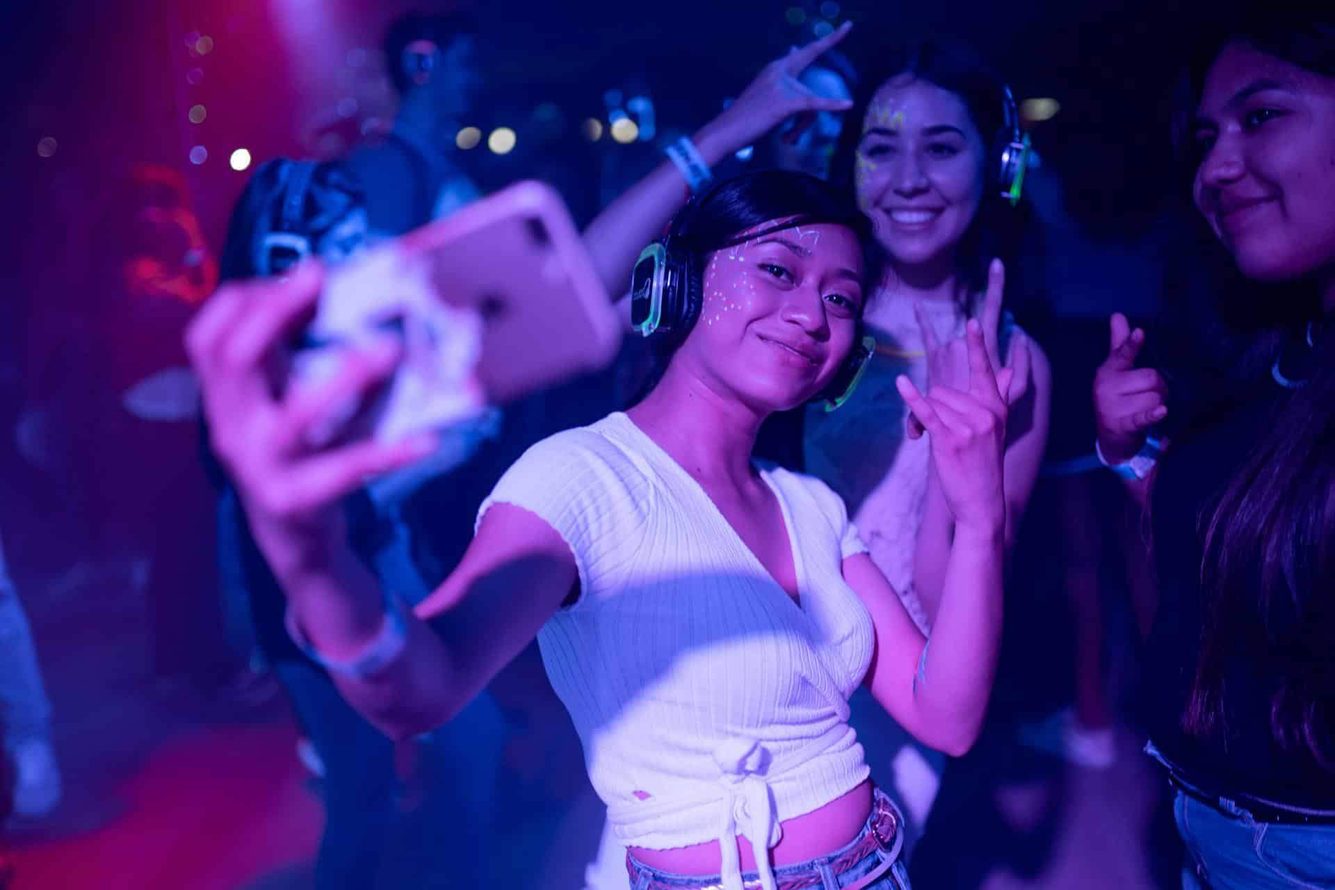 Woman in takes a selfie at futuristic party surrounded by neon lights