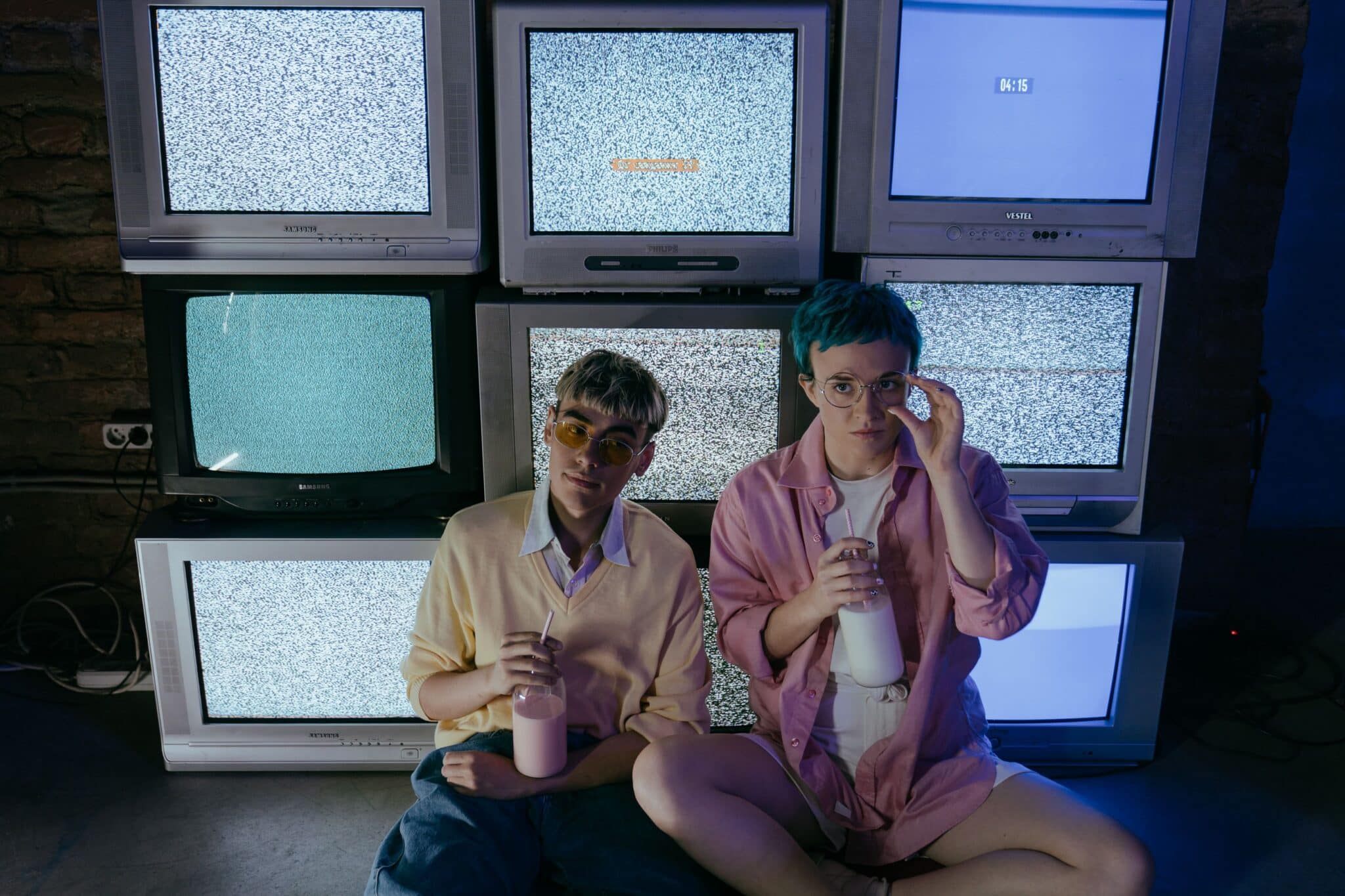 Two people sitting in front of a stack of CRT TVs