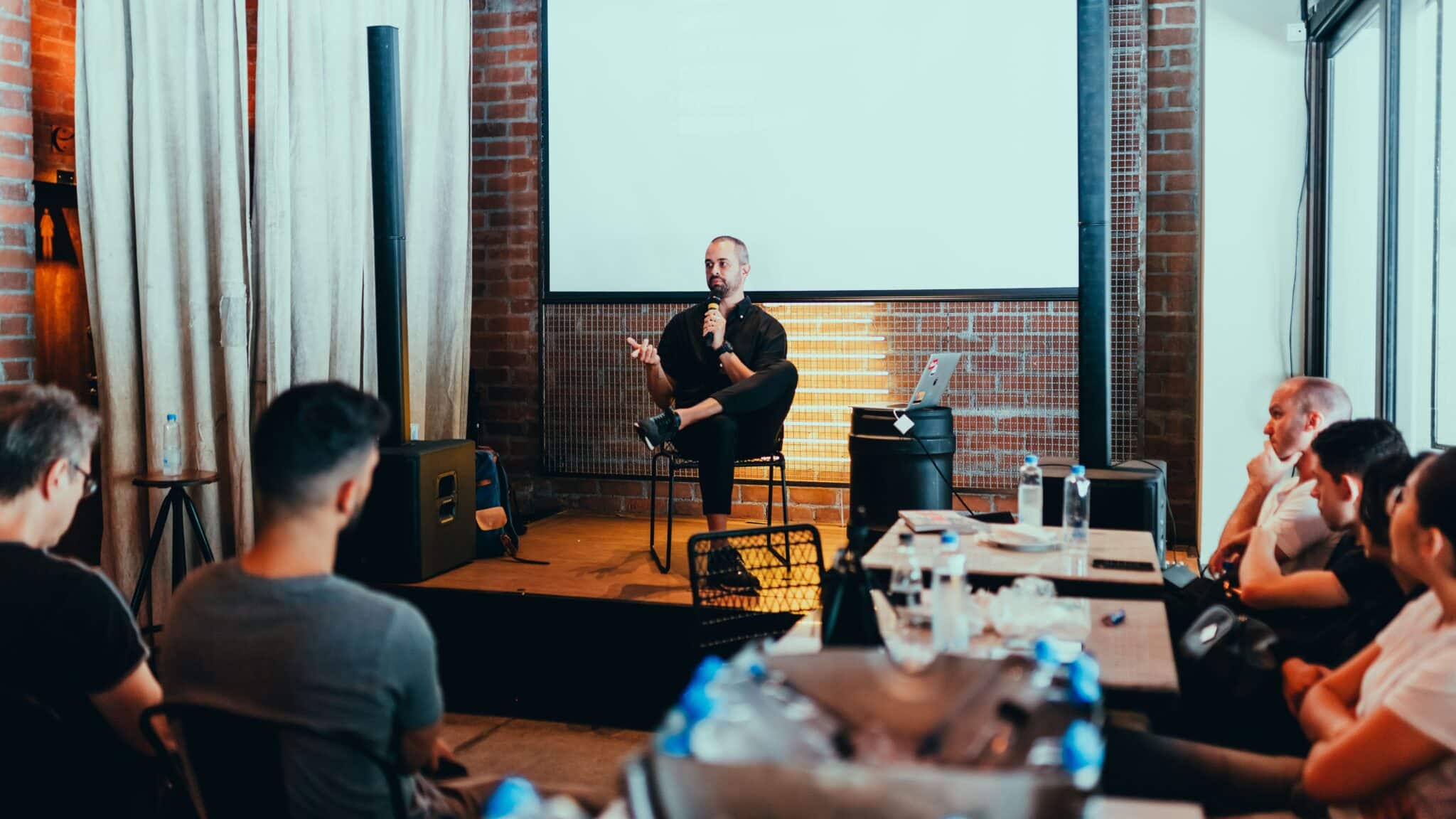Person talking on stage surrounded by a small audience